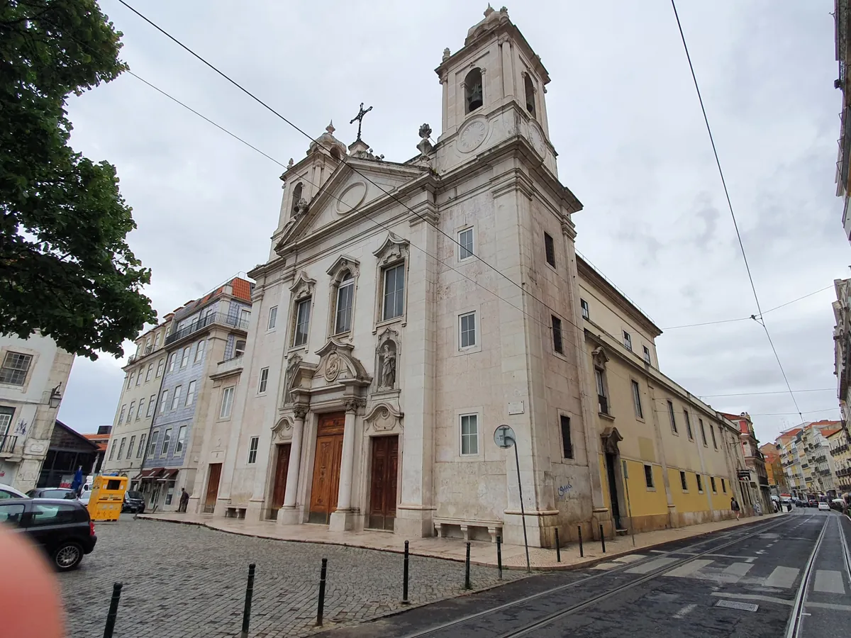 The Church of São Paulo seen from the corner of its square, one bell tower rising above a pale stone front, a yellow side wall running down the street