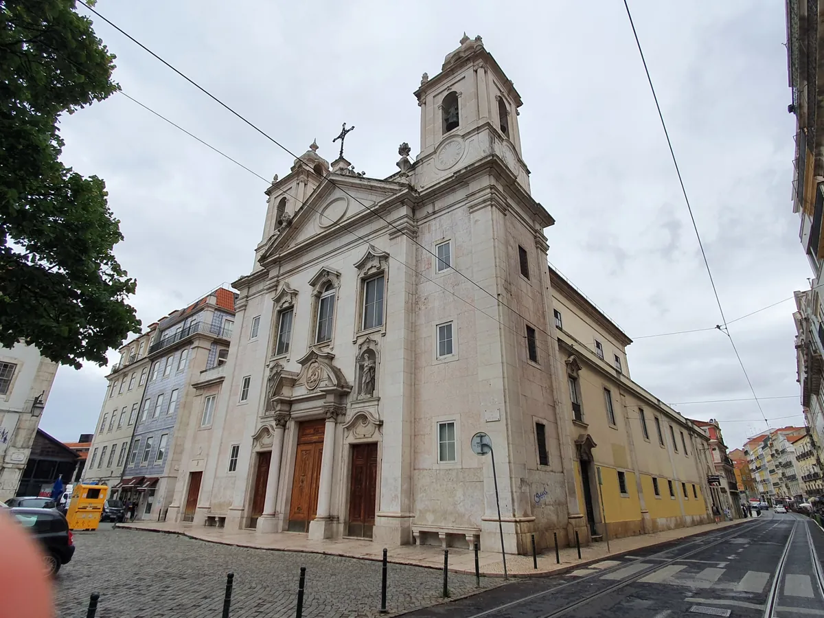 The Church of São Paulo in Lisbon seen from the side of its square under an overcast sky, a bell tower and triangular pediment above three wooden doors