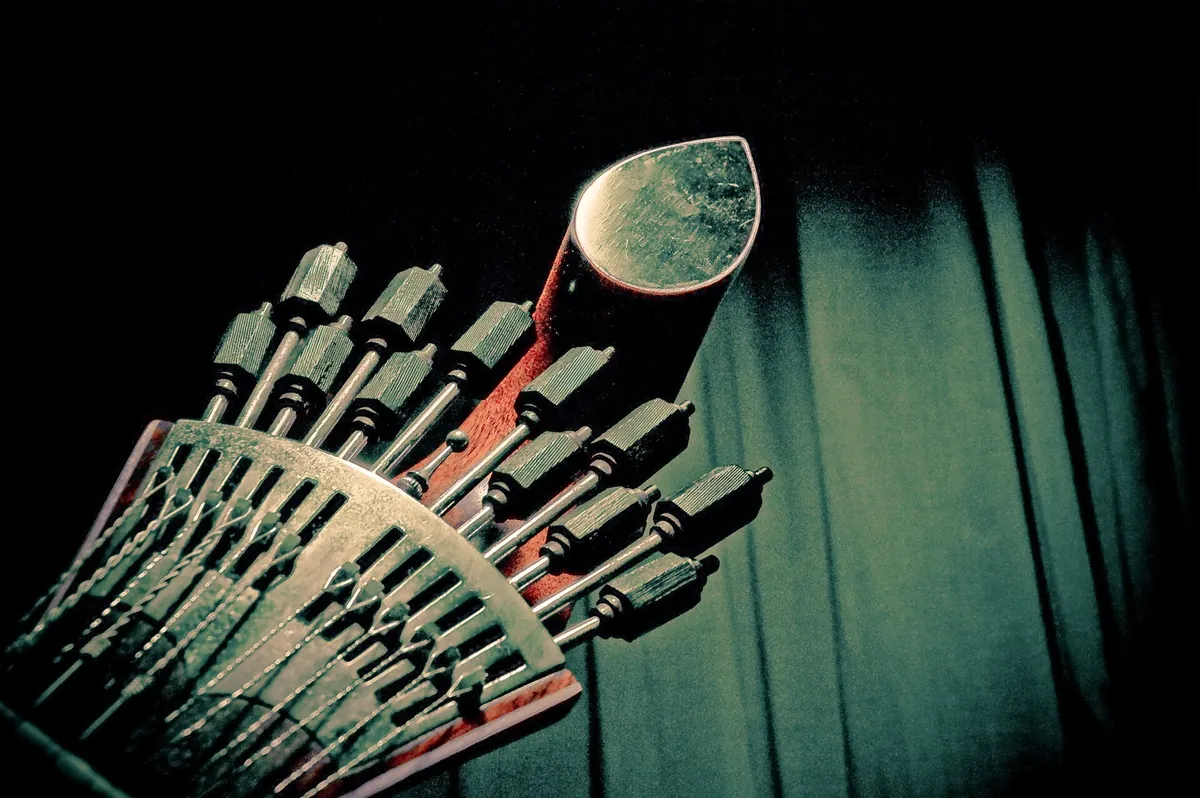 Close view of the watch-key tuning pegs at the head of a Portuguese guitar, lit in silver against a dark green background