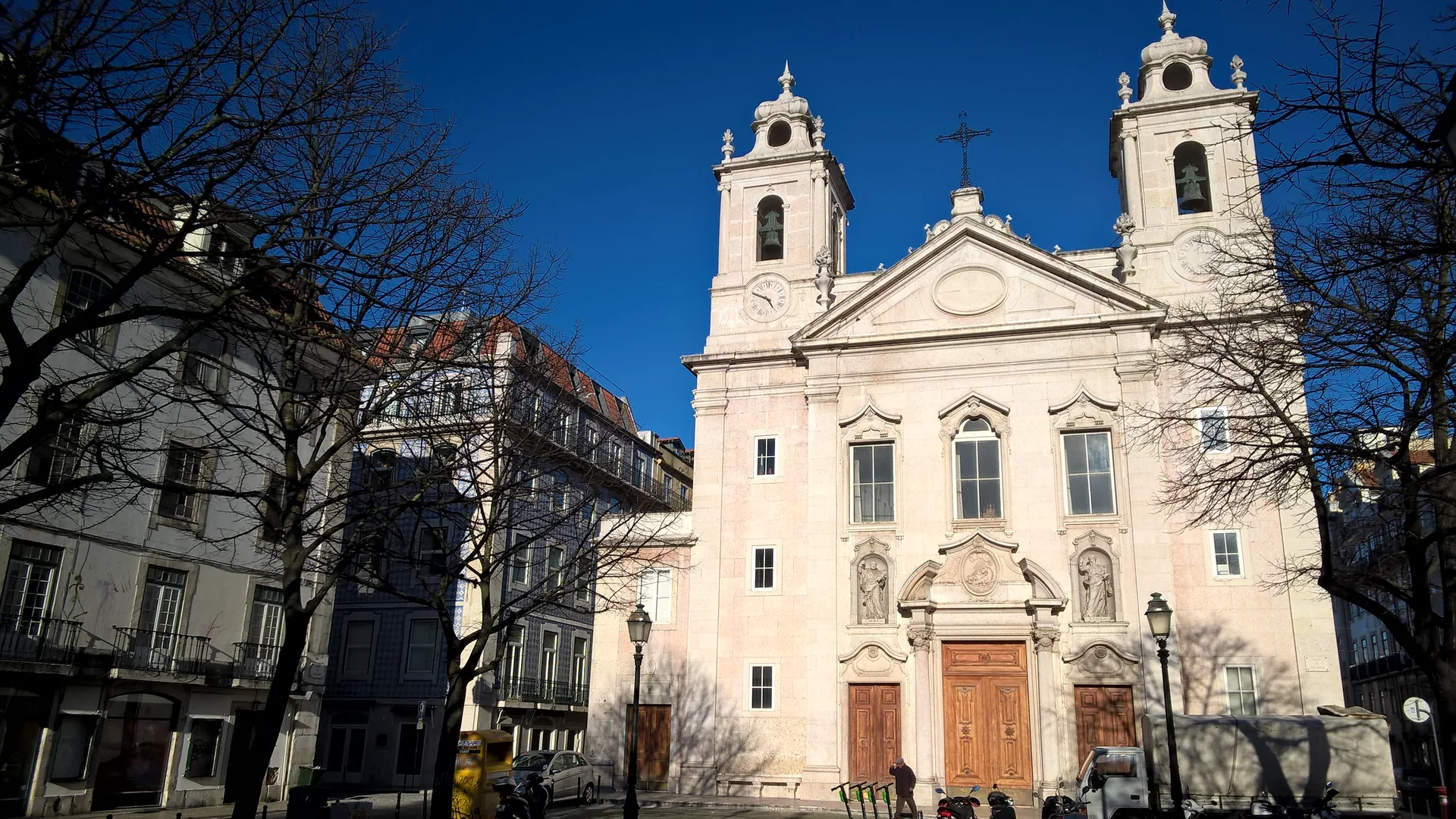The pale stone front of the Church of São Paulo in Lisbon, two bell towers above a triangular pediment, against a deep blue winter sky